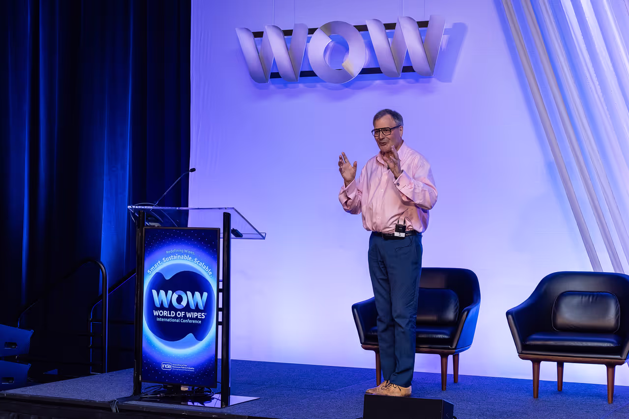David E. James presenting his paper on stage at the World of Wipes 2026 International Conference in Nashville, beside a lectern displaying the WOW World of Wipes conference branding